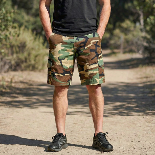 Person wearing camouflage shorts standing outdoors on a dirt path with trees in the background.